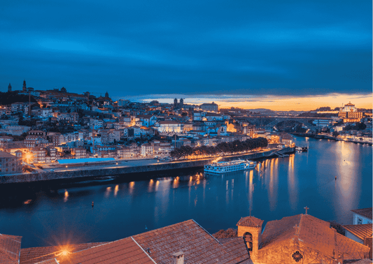 Blick auf Porto am Douro-Fluss mit beleuchteter Altstadt. Das Douro-Tal ist berühmt für Portwein und hochwertige Rotweine.